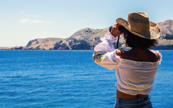 Frau schaut mit Fernglas aufs adriatische Meer
