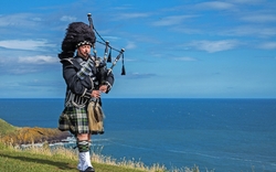 Traditionelle schottische Dudelsackspieler in voller Dresscode mit dem Meer im Hintergrund