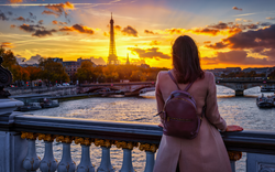 Touristin betrachtet im Herbst den Sonnenuntergang hinter der Skyline von Paris, Frankreich, mit dem Eiffelturm und der Seine