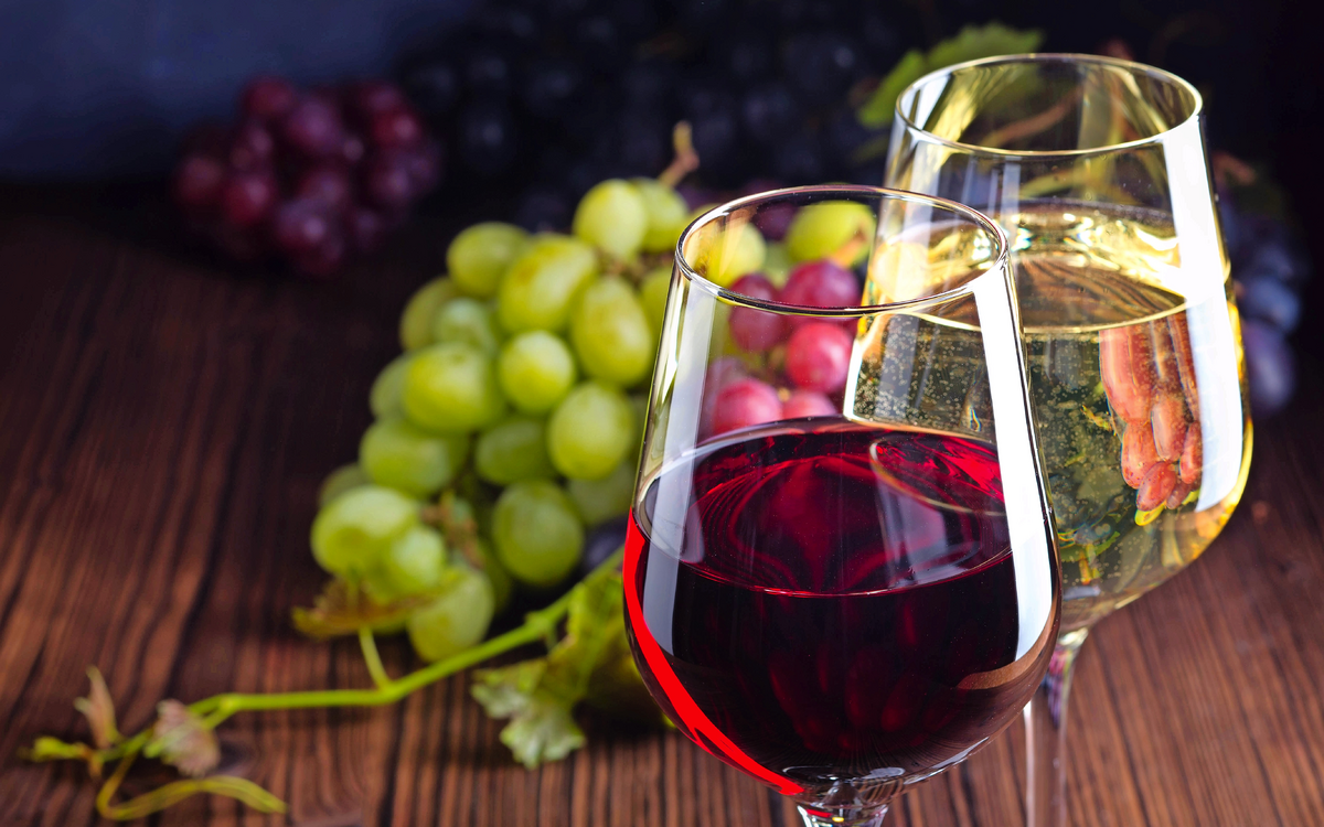Gläser mit Rot- und Weißwein mit Trauben auf hölzernem Hintergrund